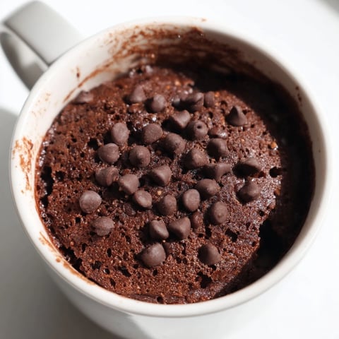 A warm, close-up shot of a rich Mug Cake Schokolade, topped with melting chocolate chips.