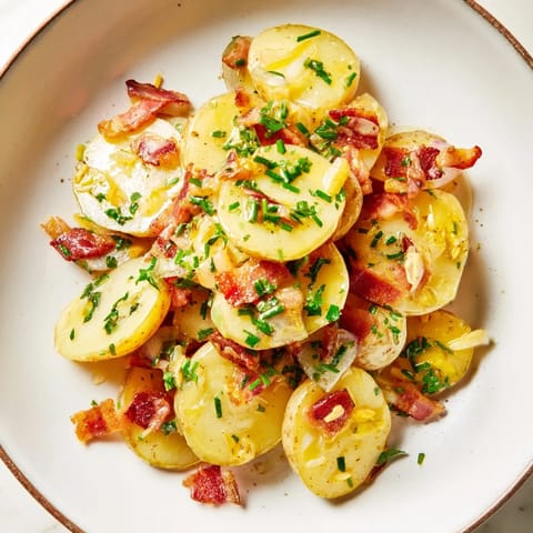 Tangy Warm German potato salad, perfectly tossed with bacon and fresh herbs in a bowl.
